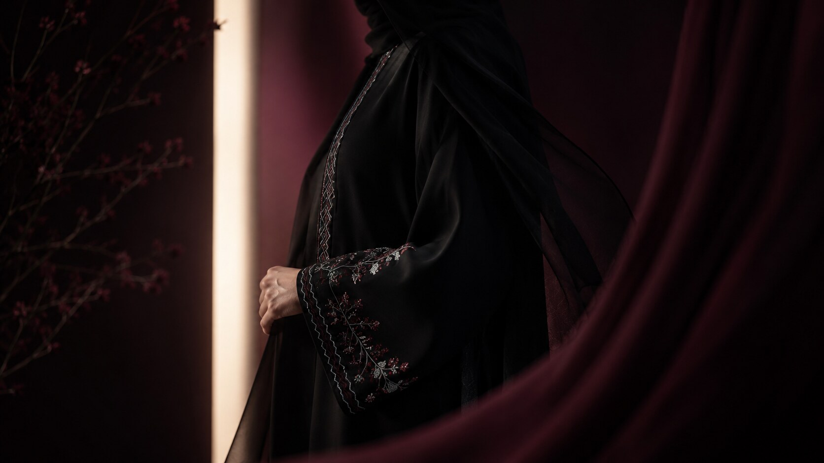 تفصيل تطريز زهري على كم عباية سوداء، في ضوء دافئ على خلفية خمرية